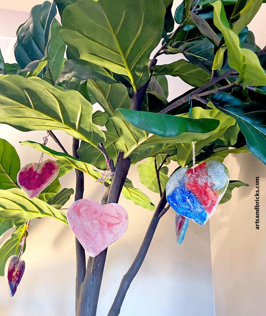Salt dough heart ornaments with glitter, paint and LEGO brick prints - displayed on a faux fiddle leaf fig tree.
